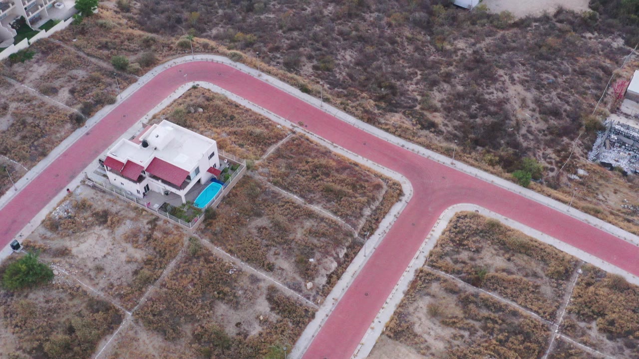 Overhead view of a house, pink road, dry fields, and nearby buildings.