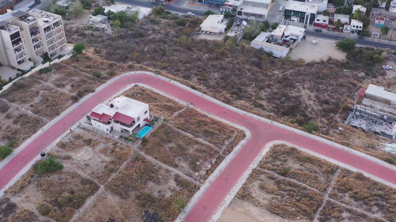 Aerial shot of dry urban fringe with red roadway and scattered buildings.