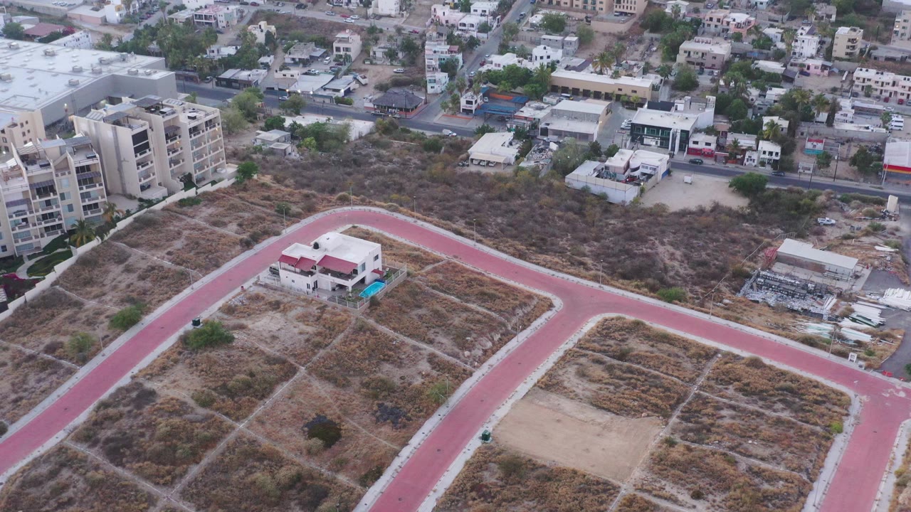Oblique drone view of a red road, open dry parcels, and dense town buildings.