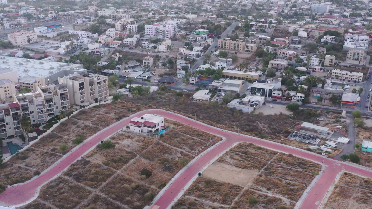 Aerial view over dry lots, curved red roads, and low-rise city buildings.
