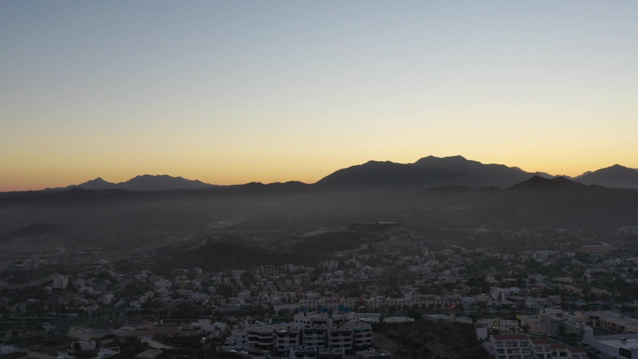 Dusk city view below mountain silhouettes and a pale sky.