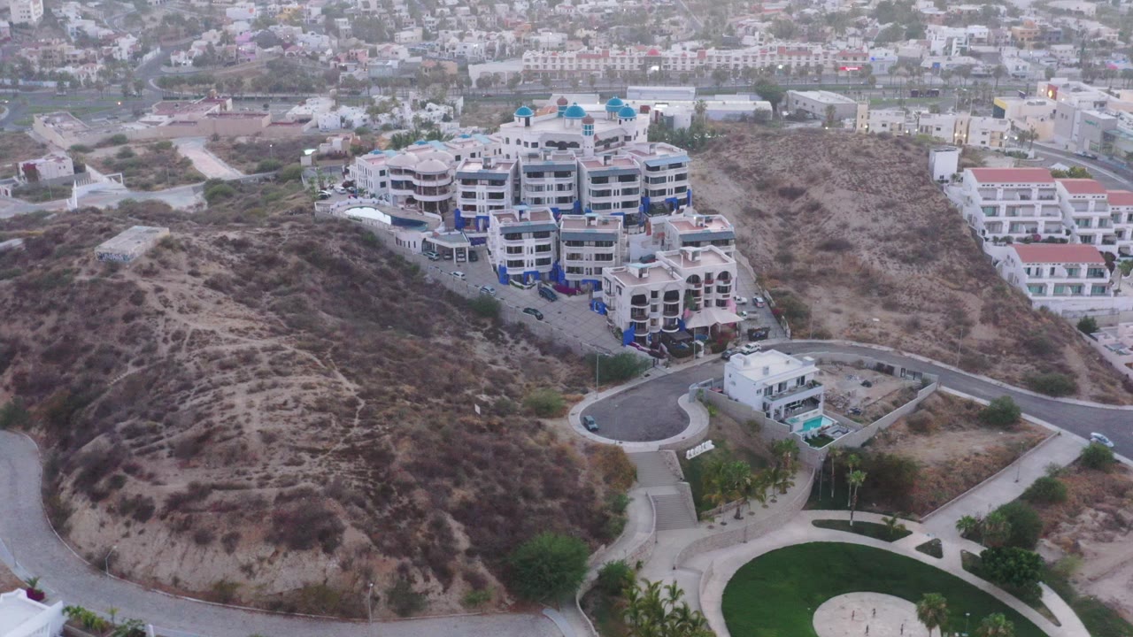 Aerial view of condominiums beside a dry hillside and curved road.