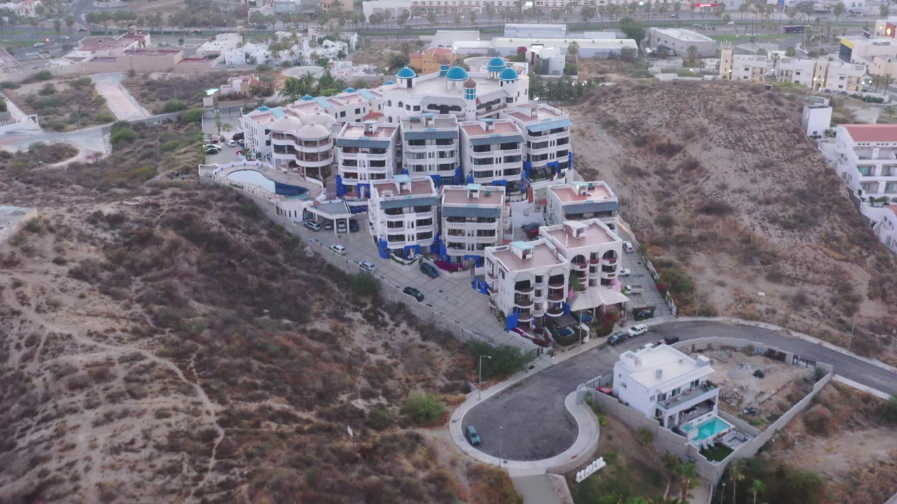 Aerial view of hillside buildings, roads, pools, and dry scrub terrain.