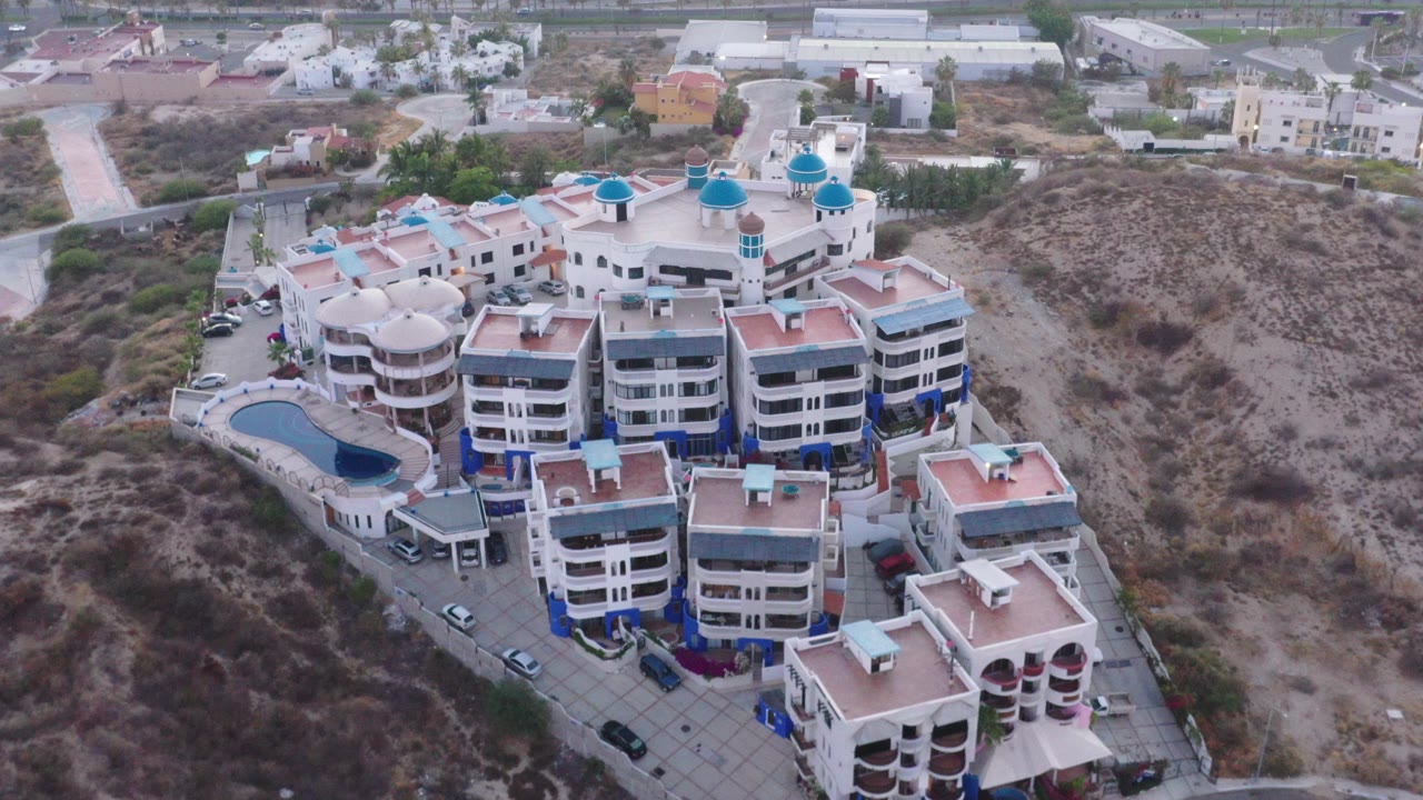 Aerial view of a white holiday complex beside dry hillside terrain.