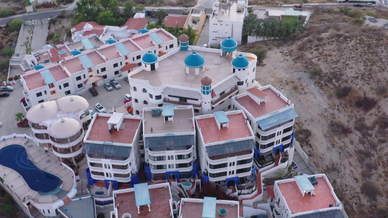 Aerial view of white buildings with red roofs and blue domed towers beside dry scrubland.