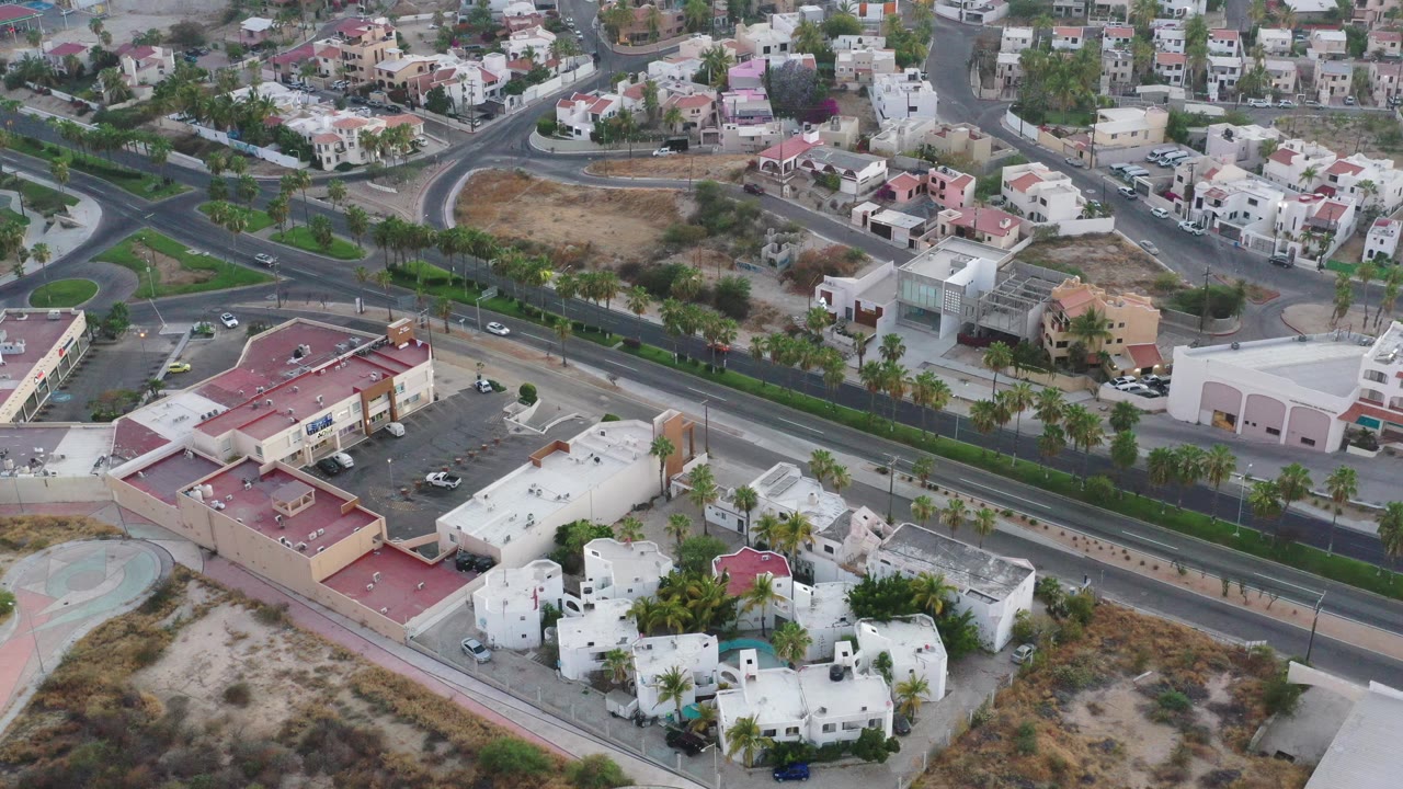Overhead view of residential blocks, a curved intersection, shops, medians, and traffic.