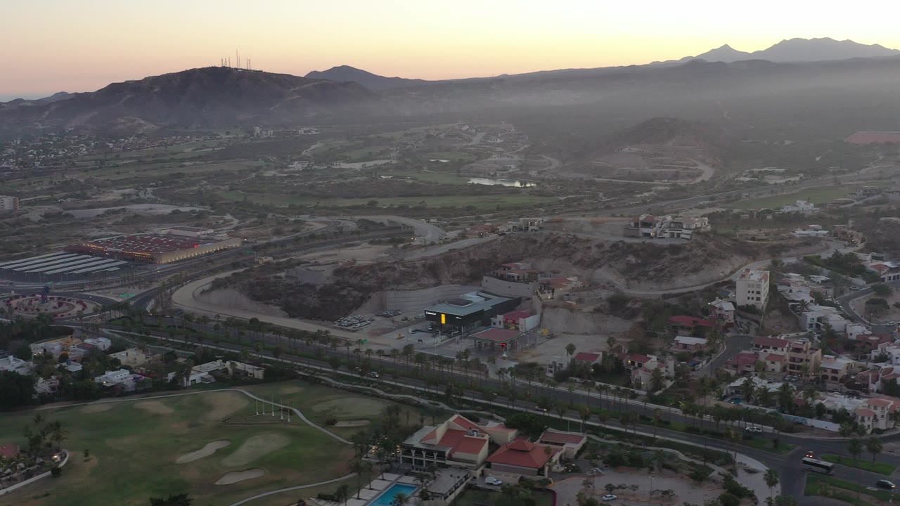 Aerial view of homes, roads, green grounds, and mountains at sunset.
