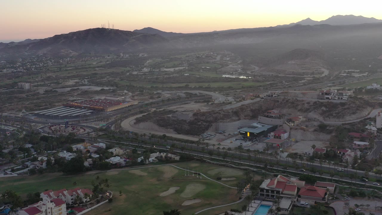 Aerial view of golf course, roads, buildings, hills, and mountains at low light.