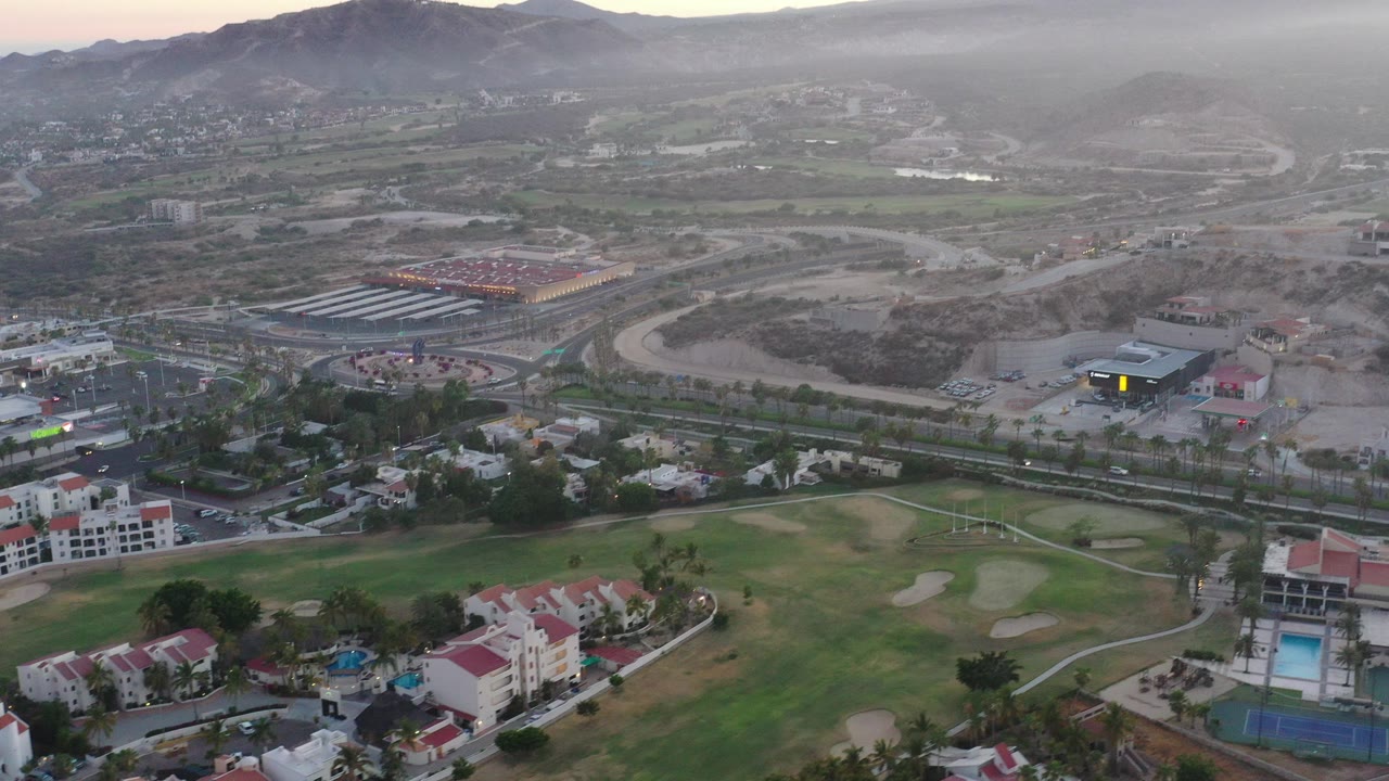 Aerial view of red-roofed homes, green open space, roads, and hazy hills.