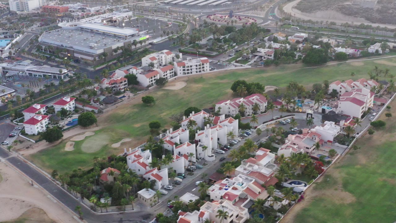 Aerial view across red-roofed housing, green fairways, and roadways.