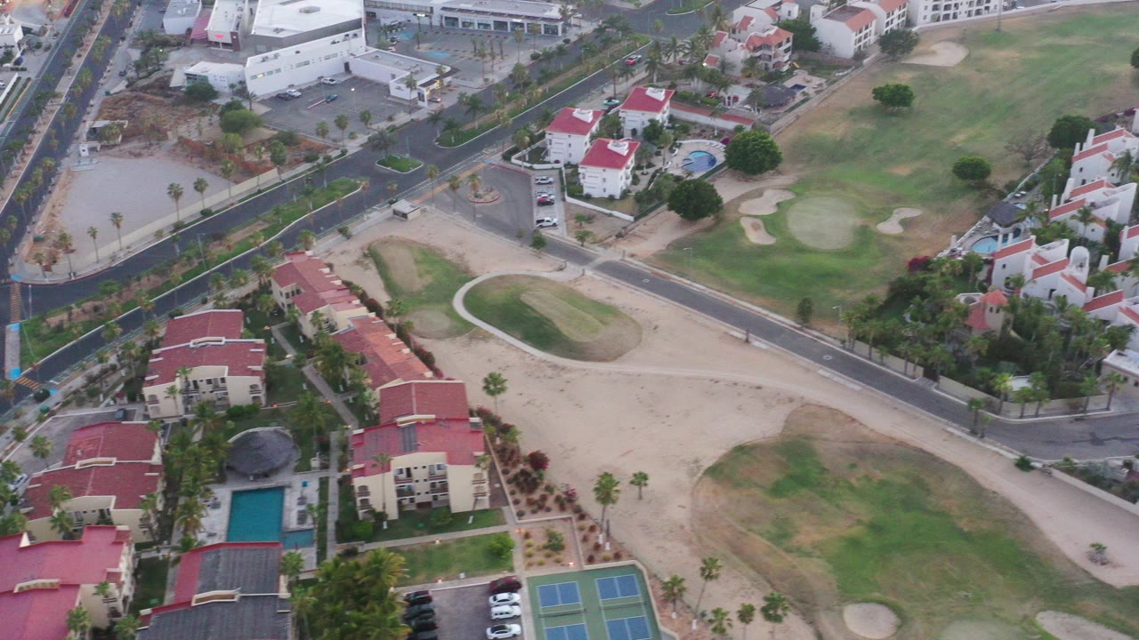 Aerial view of red-roofed buildings, pool, tennis courts, roads, and golf-course sand.
