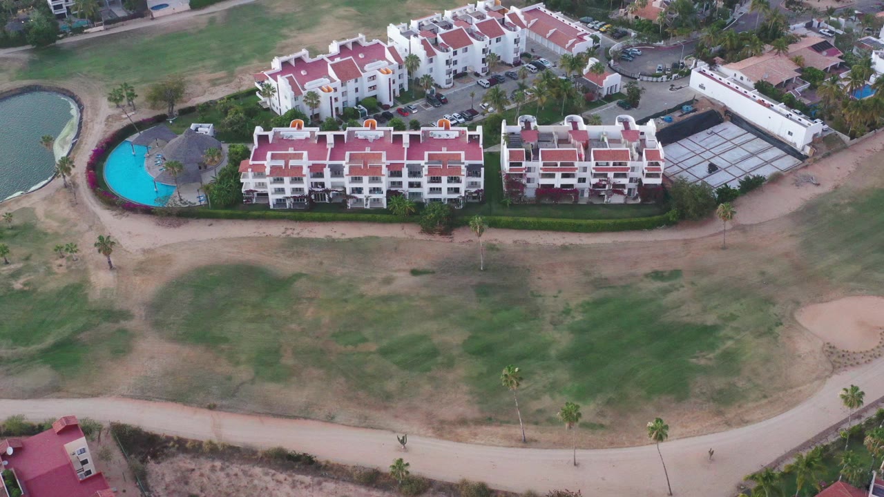 Aerial neighborhood view with red roofs, pool, pond, and open lawns.
