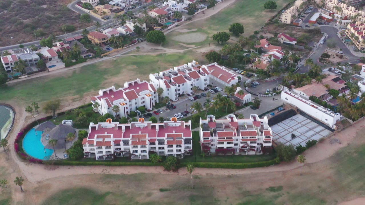 Drone-style overhead view of condo buildings, green grounds, and dry hillside neighborhood.