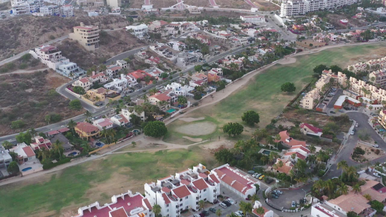 Residential rooftops and hillside buildings seen from above with green space nearby.