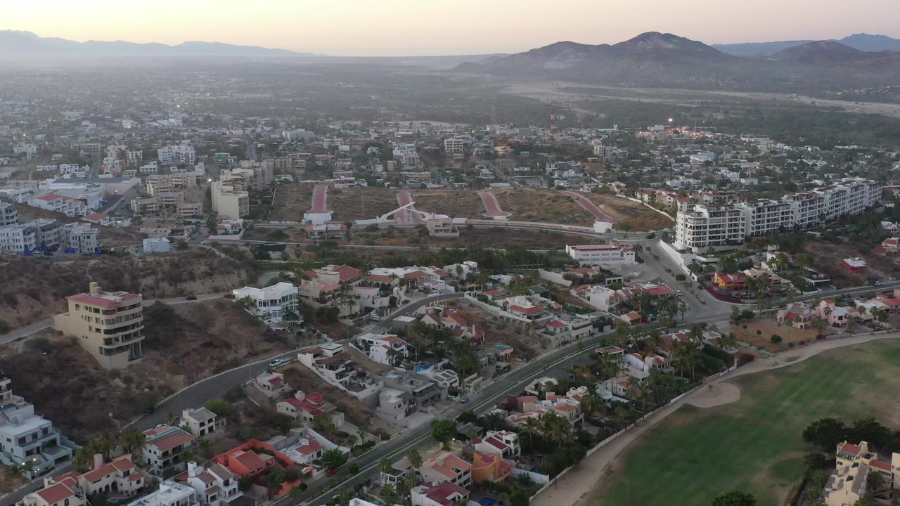 Drone-like town panorama with houses, roads, green space, and hills in the distance.