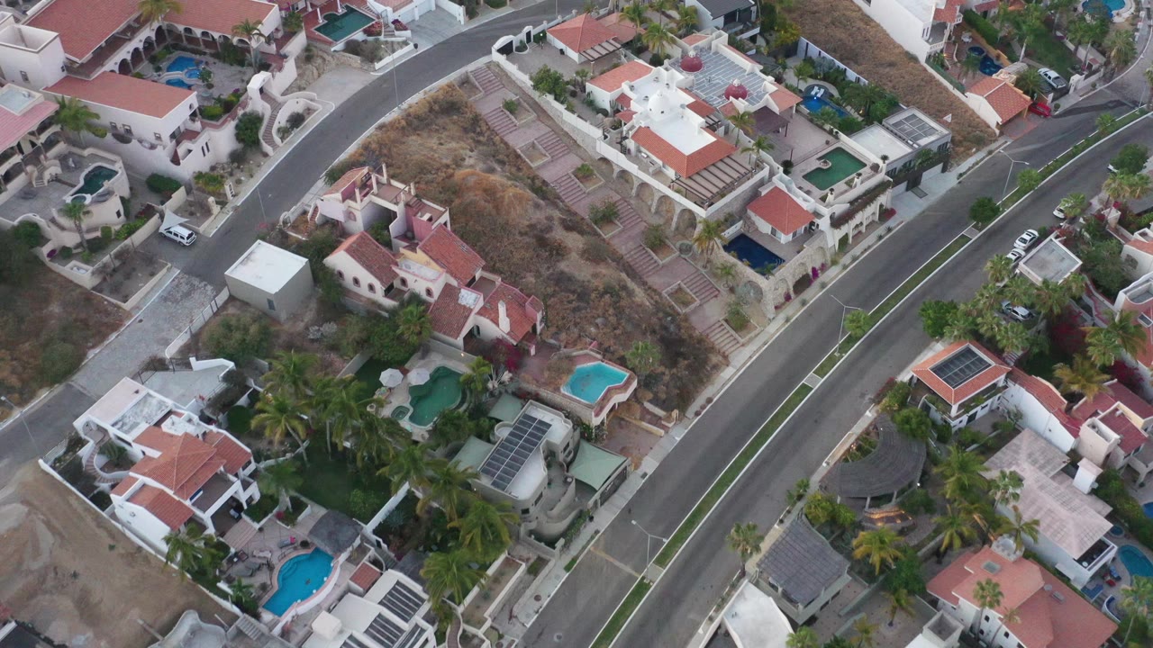 Drone-like overhead angle on houses, pools, and a quiet road.
