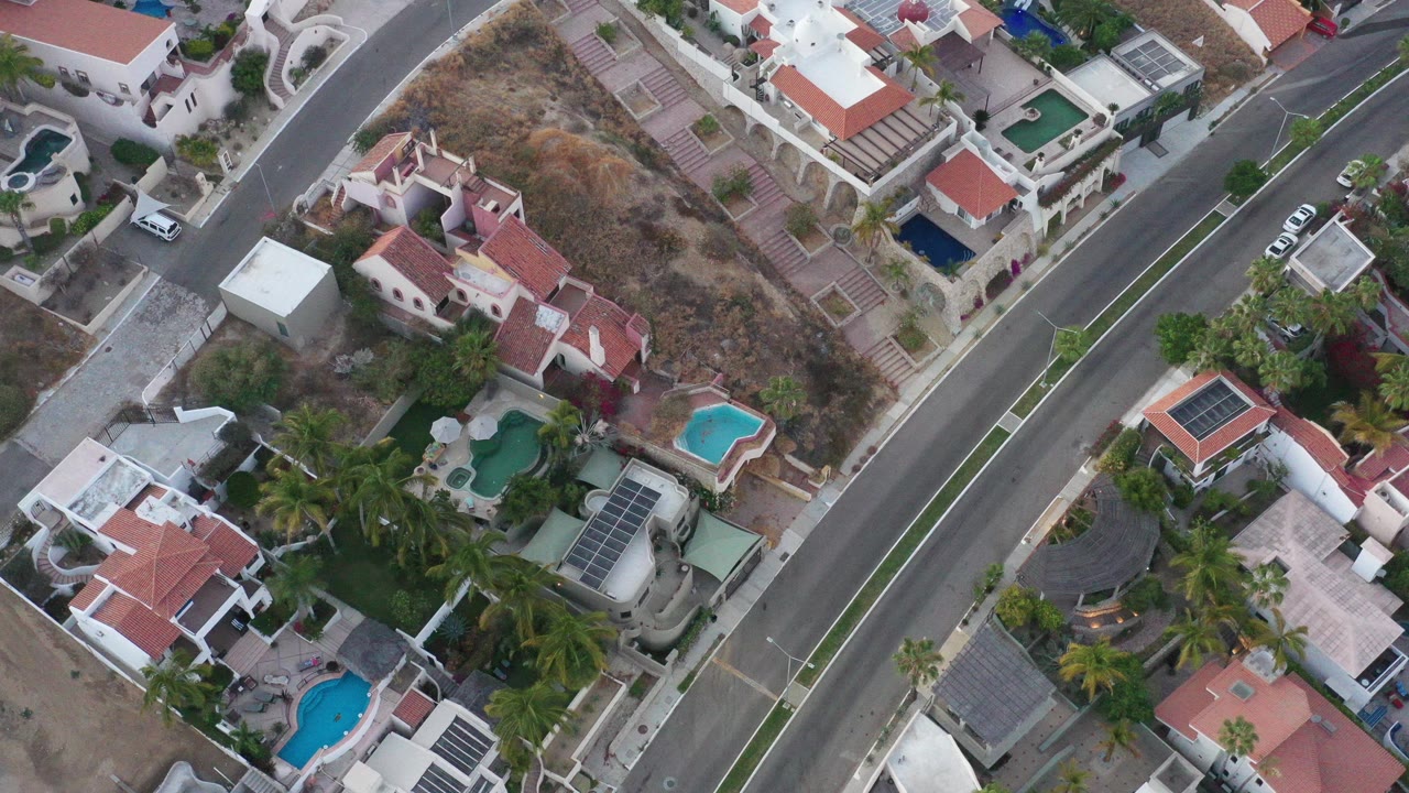 Overhead view of homes, pools, palms, and a divided road.