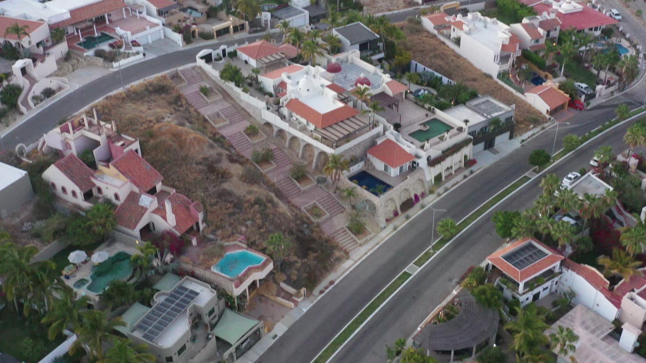 Aerial view of villas, pools, palms, and a curving road.