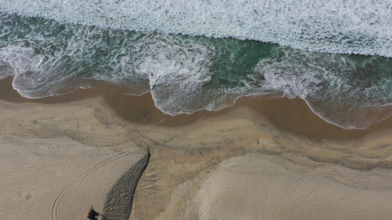 Aerial beach view with surf and patterned sand.