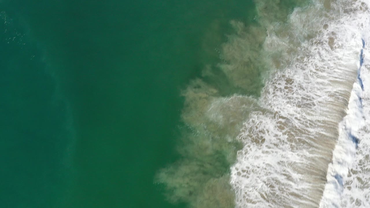 Overhead green ocean water with white surf and sand churn.