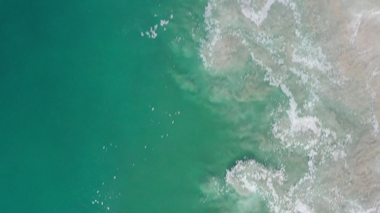 Aerial view in Los Cabos, Mexico, showing green-blue ocean, pale coastal rock, thin white wave wash, and no visible people.