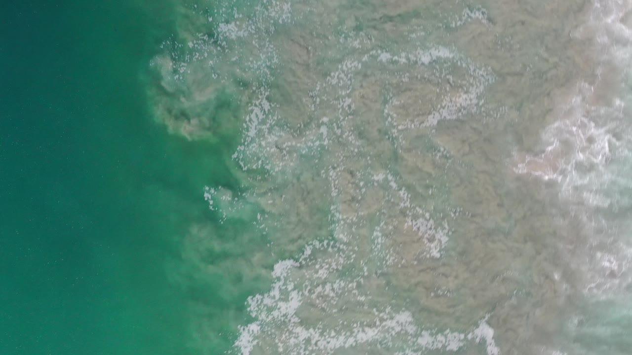 Turquoise ocean edge with irregular white wave foam on shore.
