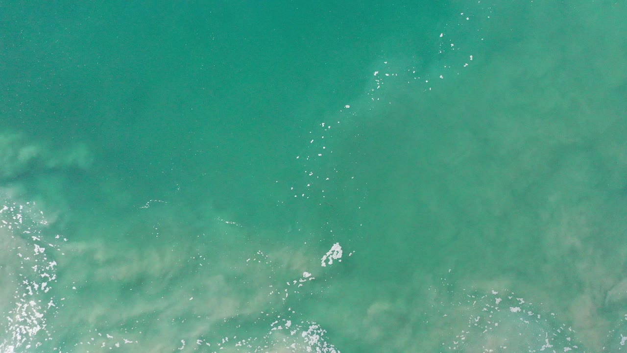 Overhead view of light green seawater in Los Cabos with pale underwater haze, small white foam marks, and no visible people.