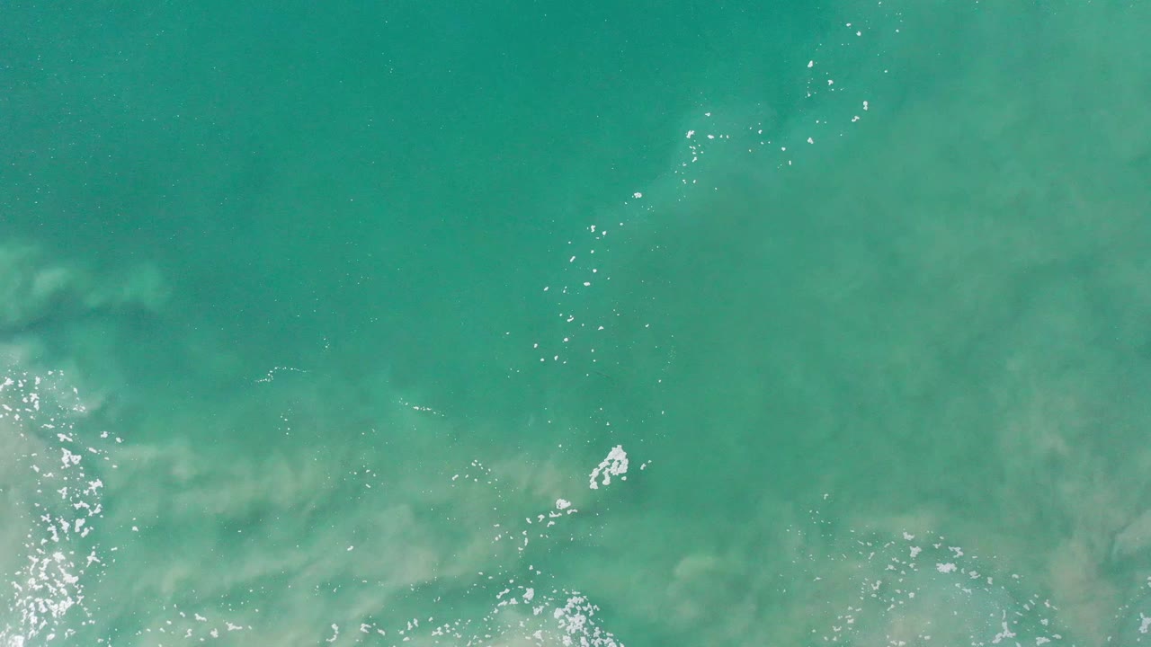 Light green Los Cabos sea surface seen from above, with bright reflection clusters near the lower center and no visible people.