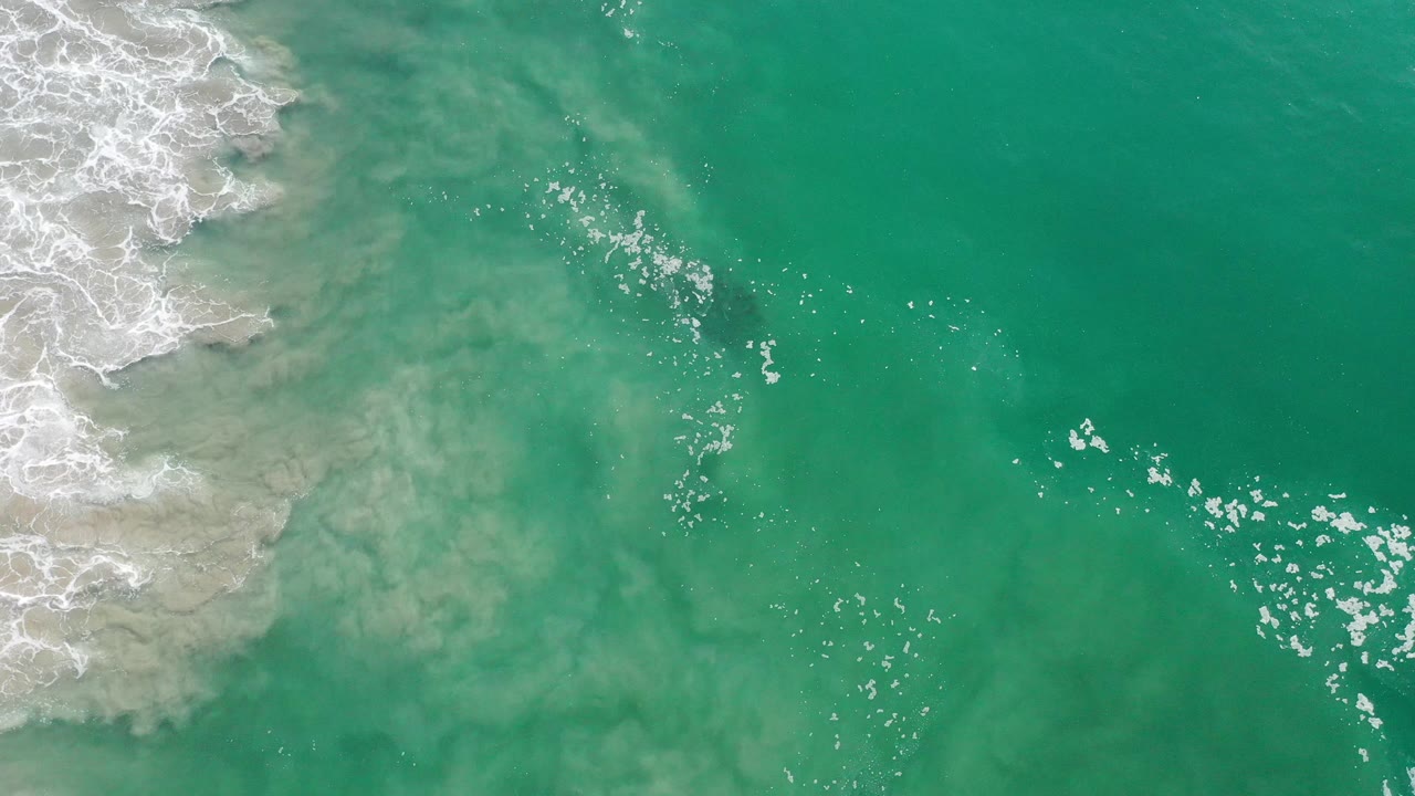 Green-blue ocean viewed from above with surf foam at the upper left.