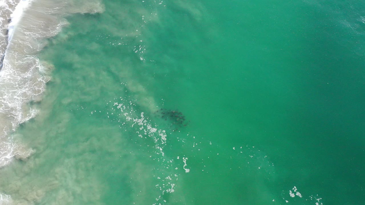 Overhead green seawater with surf wash at the left edge and a dark patch below the surface.