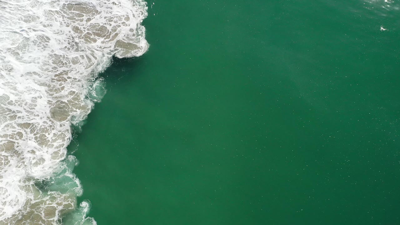 Foamy surf curls into teal water from the upper left.