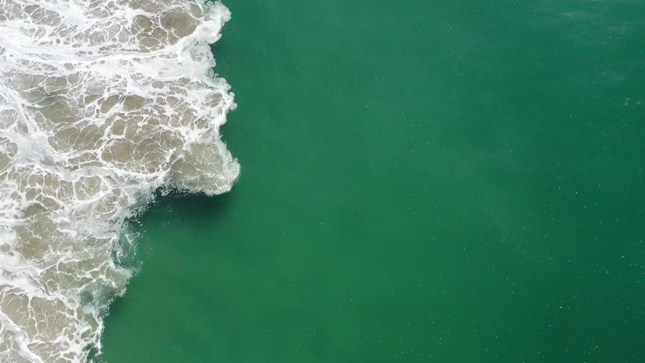 Overhead view of white surf meeting green ocean water.