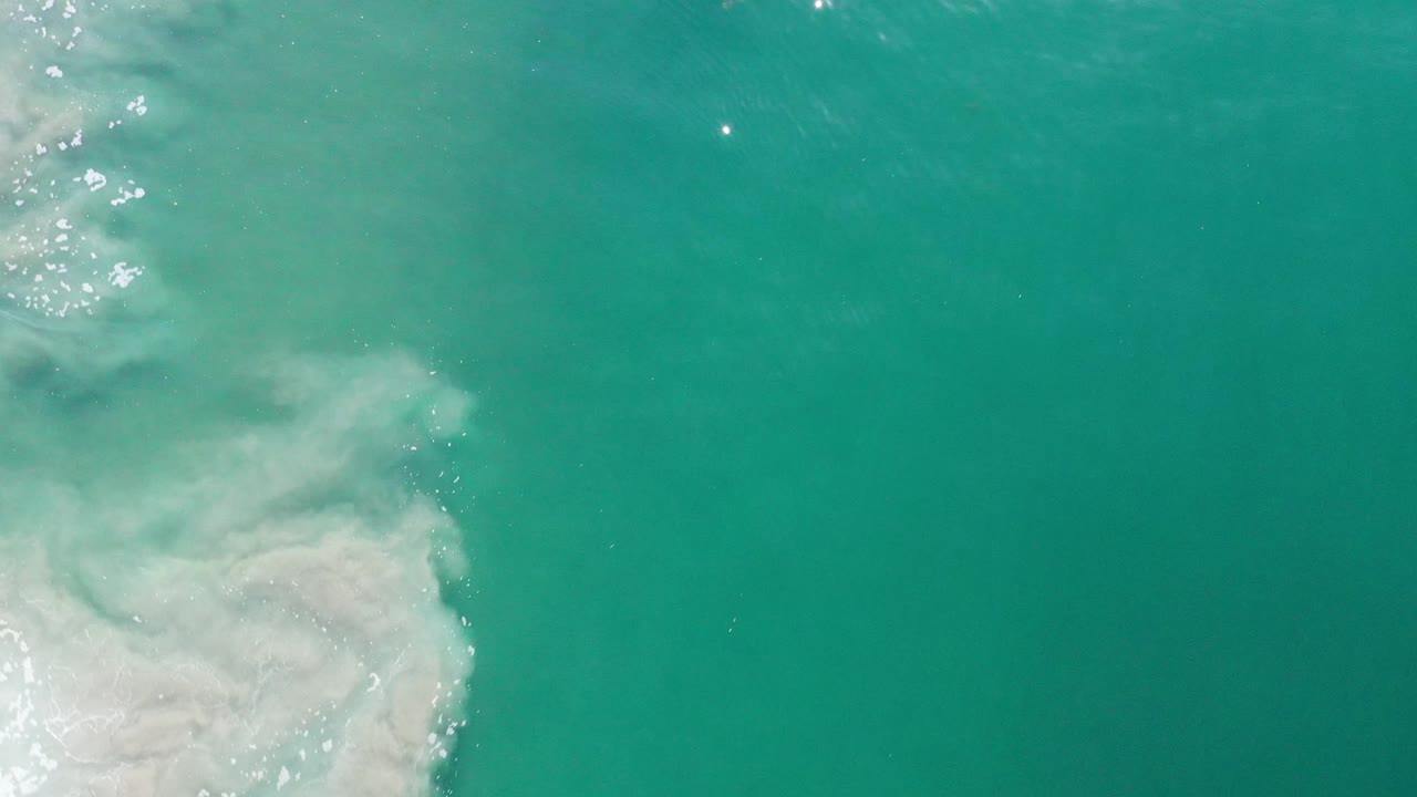 Open turquoise water with a wave edge and bright reflections near the upper left.