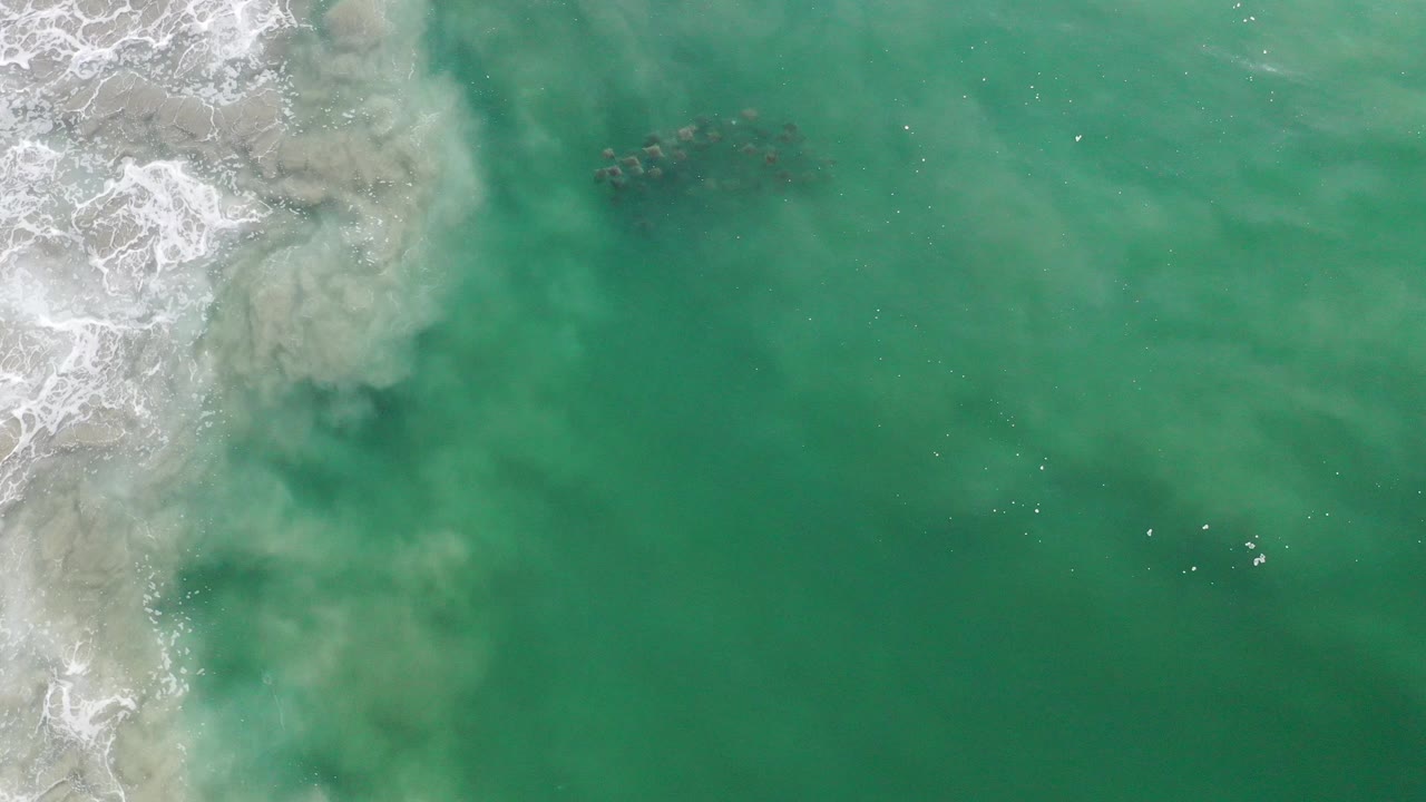 Overhead teal ocean with surf and a small dark school of fish