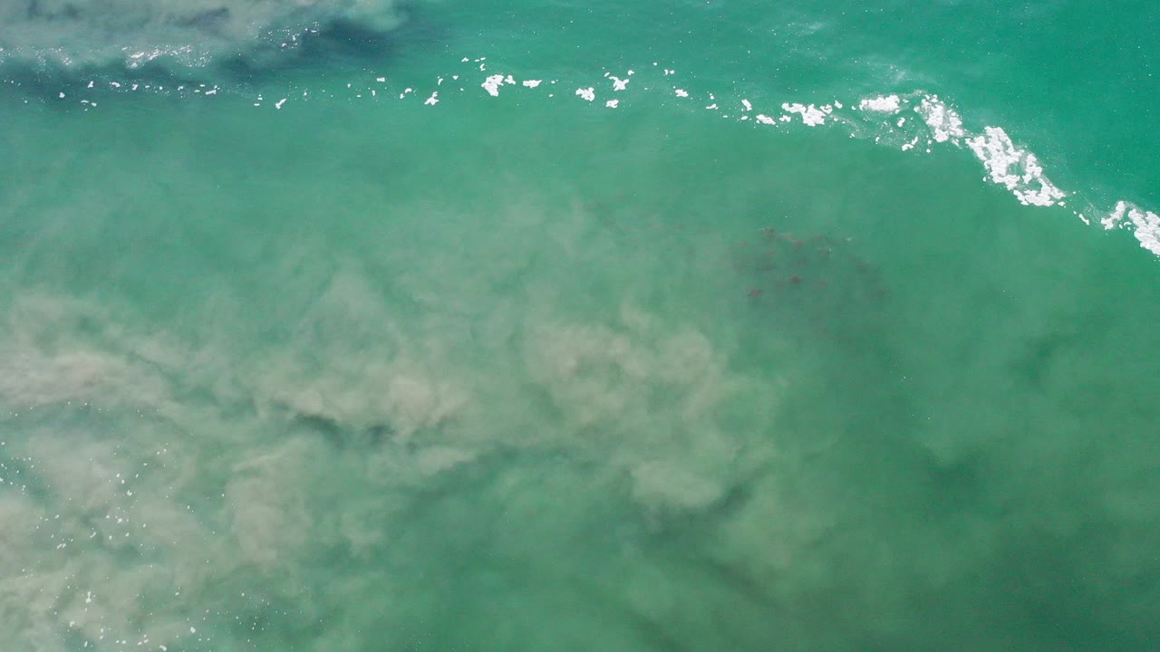 Turquoise green seawater with white foam and cloudy sand below.