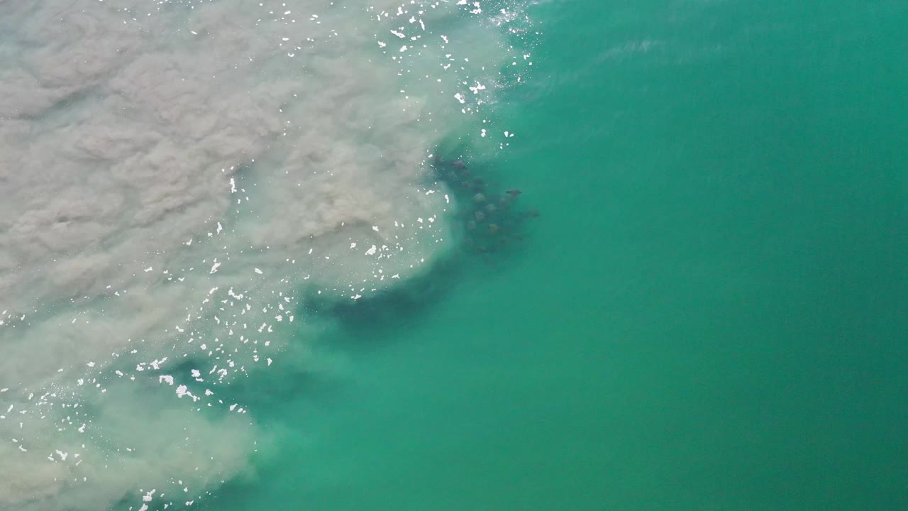 A second overhead frame shows the white foam line spreading farther across aqua Los Cabos water, with no visible people.