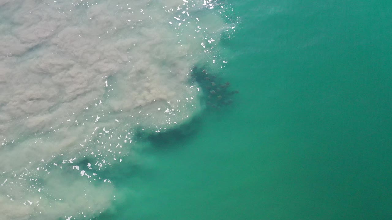 Aqua water and broken white foam beside a pale coastal edge.