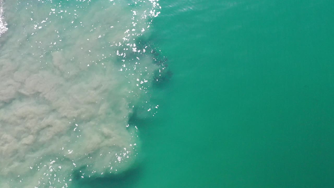 Teal ocean surface with pale underwater clouding and bright sun glitter.