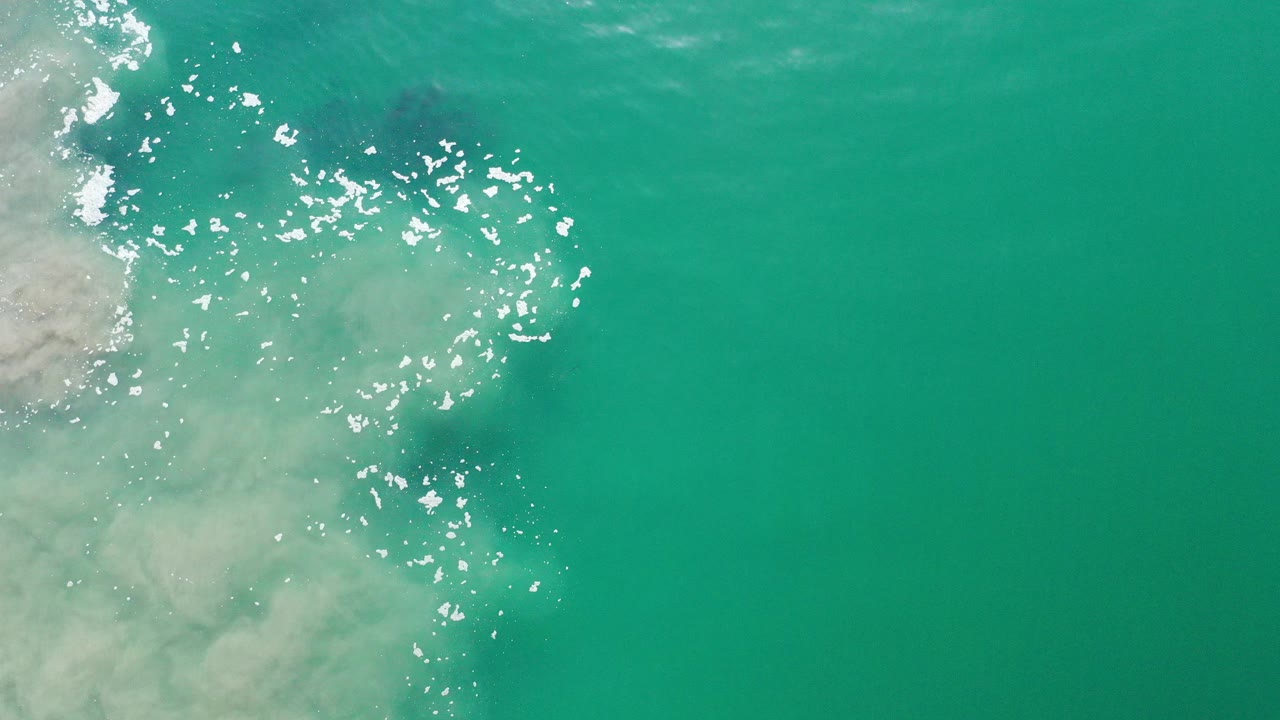 Overhead turquoise ocean water with sun glints and pale wash at left.