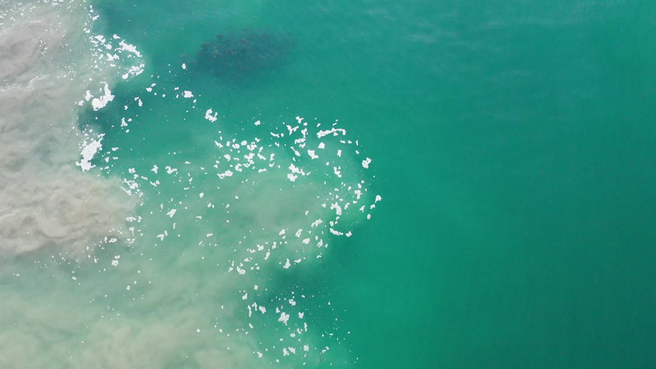 Turquoise water seen from above with foam texture and scattered highlights.