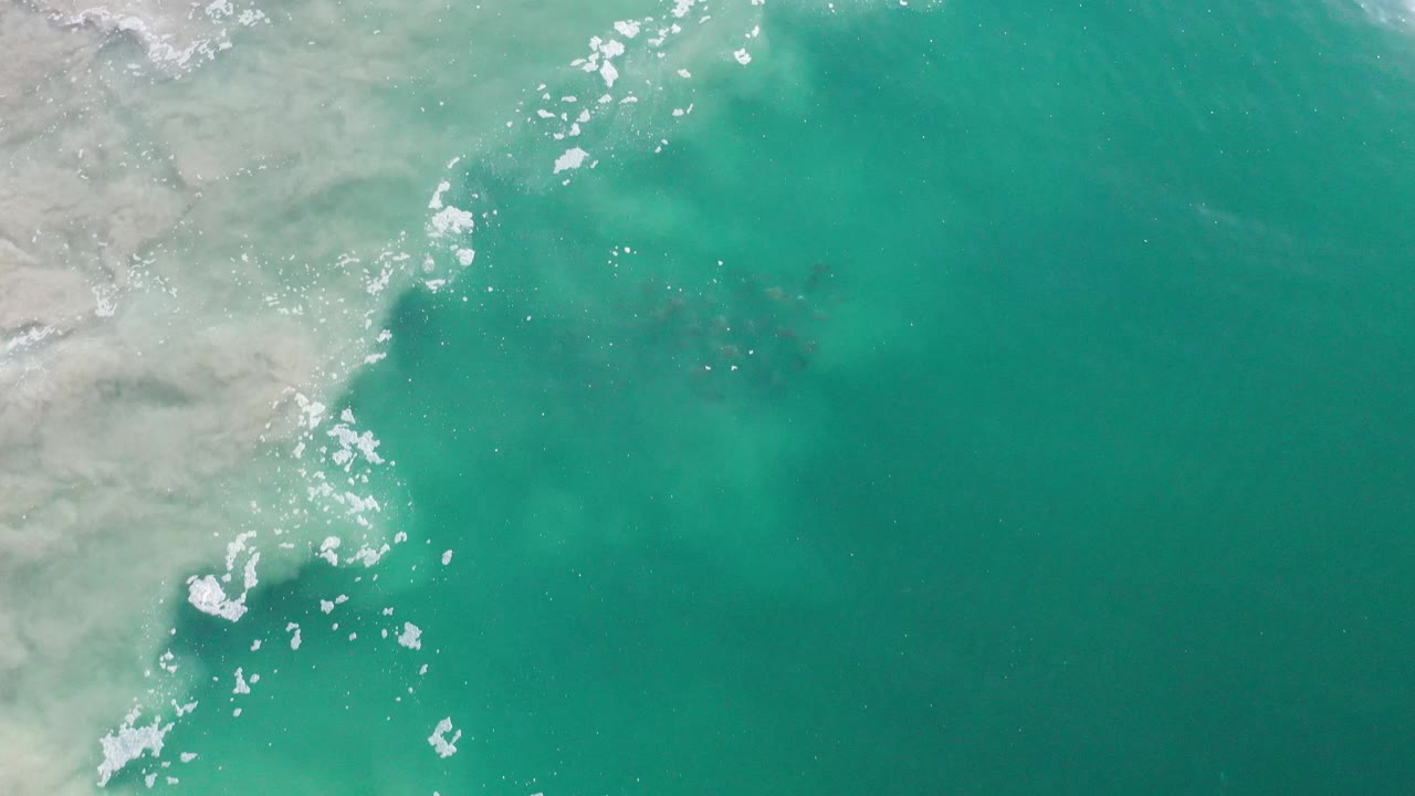 Green water and pale sand with broken white foam near the shore.