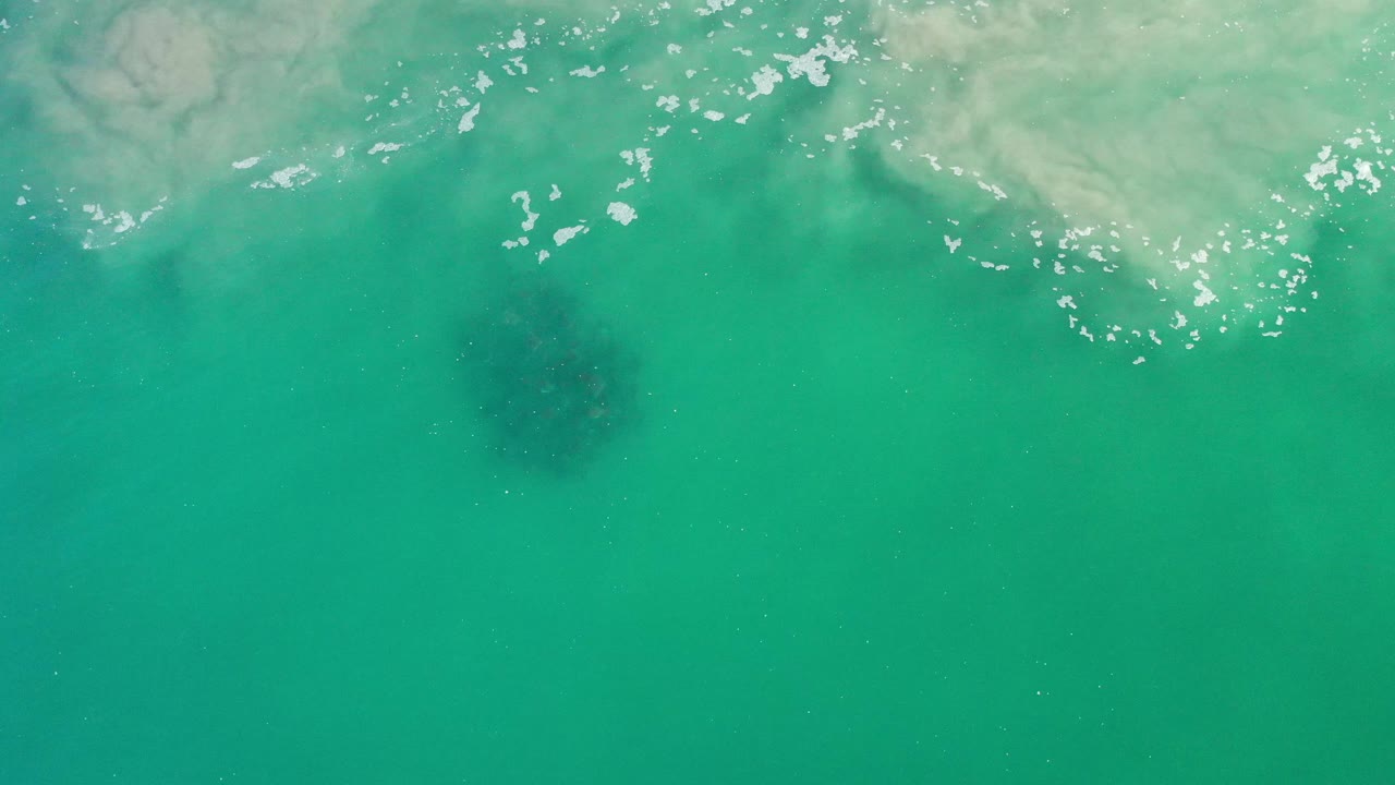 Green sea surface with pale surf texture and underwater seaweed shadow.
