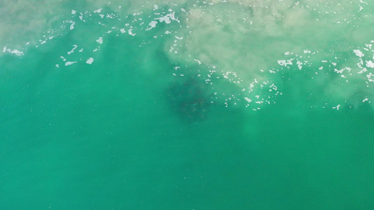 Turquoise water with white bubbles and a dark fish school below the surface.