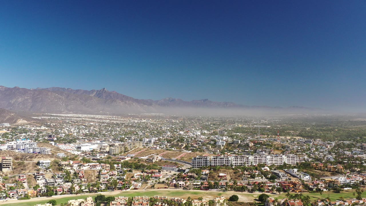 Wide aerial view over homes and hills beneath a blue sky.