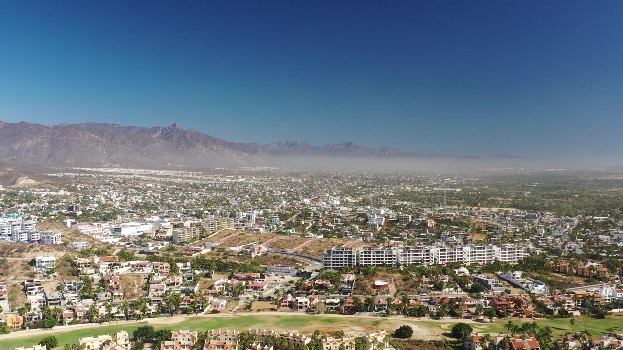 Wide aerial view of a town below dry mountains and blue sky.