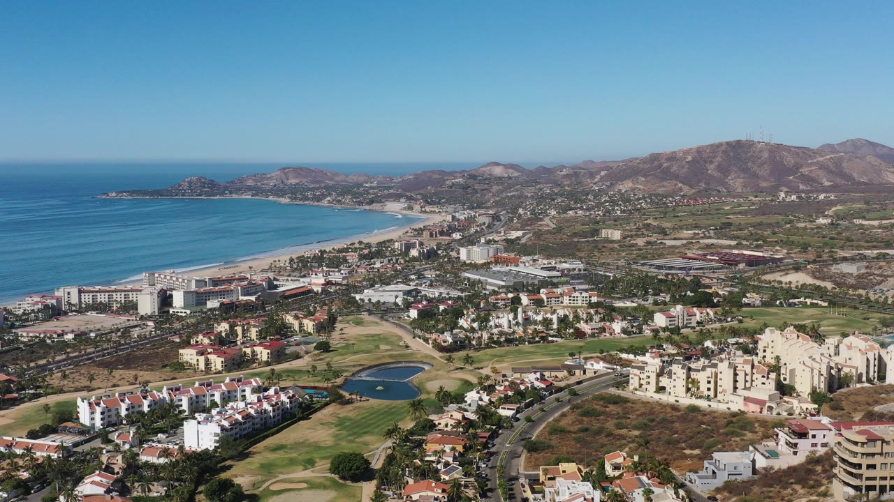 Aerial view of ocean, beach, city buildings, golf course, and hills.