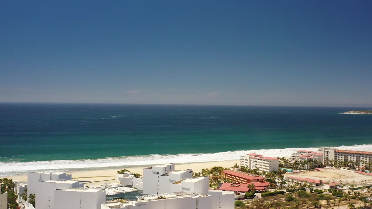 Ocean horizon above surf, sand, and beachfront buildings.
