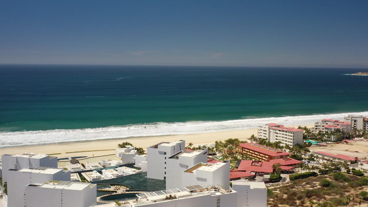 Elevated view of white buildings, red roofs, beach, surf, and ocean.