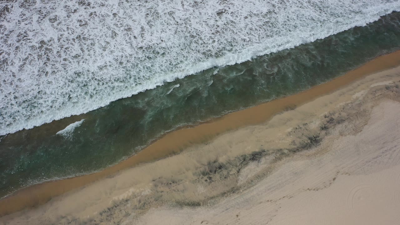 Foamy wave edge stretches across the upper frame above empty sand.