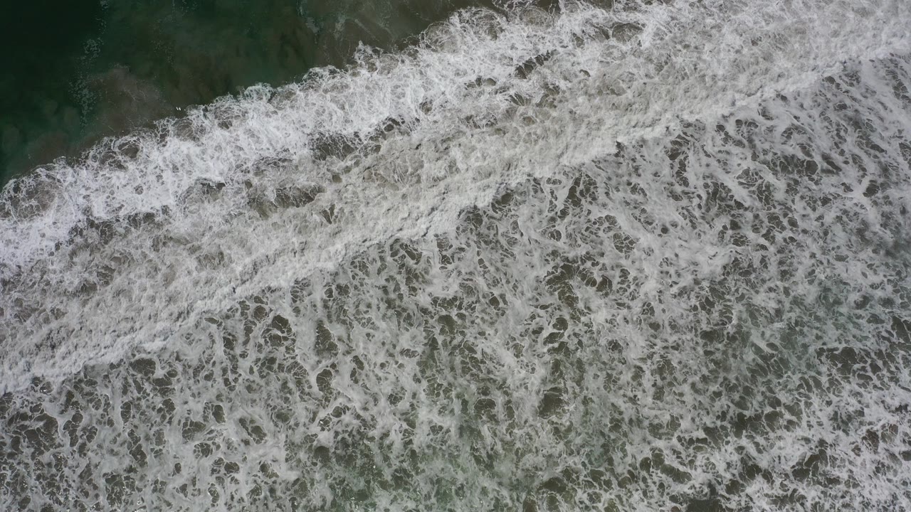 Overhead frame of white surf spreading across dark green water in Los Cabos, Mexico, with no visible people.